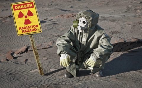 Scientist in protective suit and gas mask sitting on slag