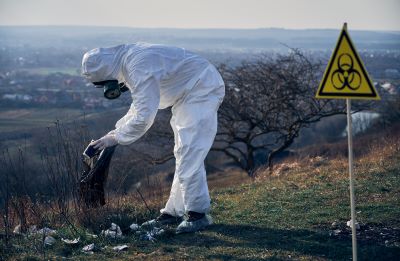 researcher protective suit collecting plastic garbage into black waste bag outdoors sunny day